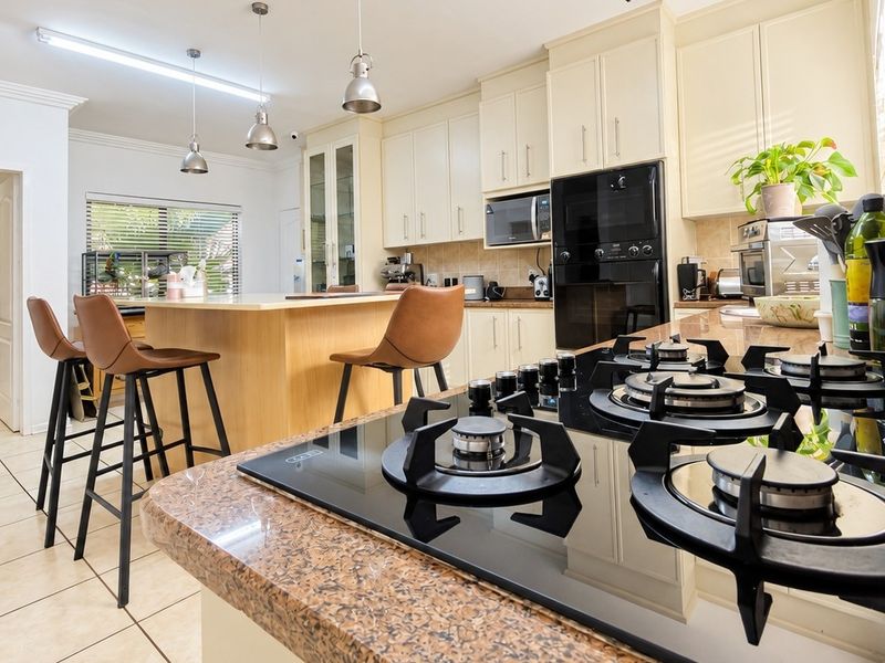 Spacious kitchen featuring granite countertops, a central island, built-in gas hob, and integrated oven, complemented by ample cabinetry and tiled flooring.
