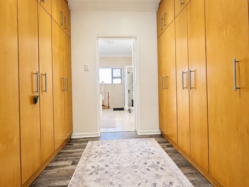 A well-maintained hallway featuring extensive floor-to-ceiling built-in wooden cabinetry and modern laminate flooring, leading directly into an adjacent bathroom.