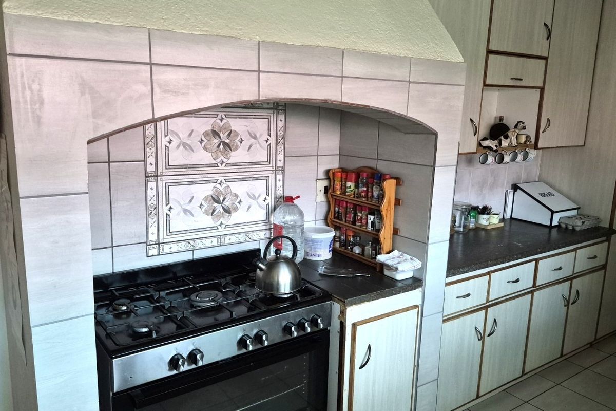 A functional kitchen featuring a built-in gas stove with an arched tiled hood, ample cabinetry, and tiled flooring, offering a classic, dated aesthetic.