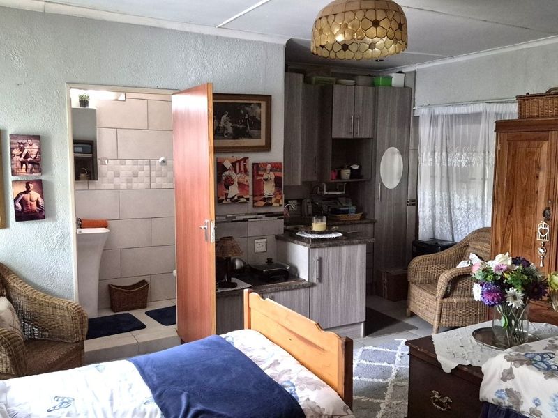 Open-plan living space featuring a compact kitchenette with built-in cabinetry and an adjoining bathroom with a pedestal basin.