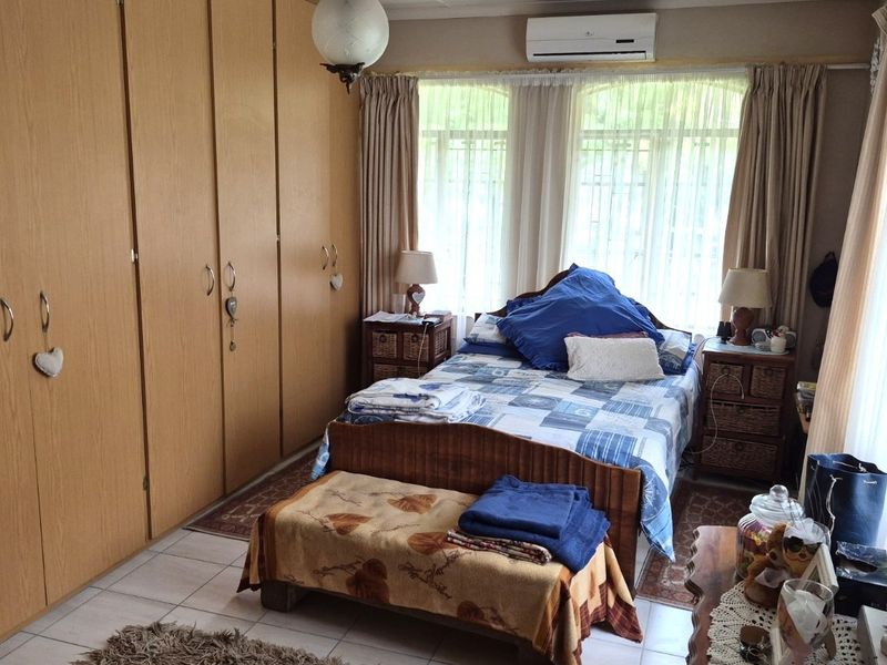 A functional bedroom featuring extensive built-in wooden cupboards, tiled flooring, and a wall-mounted air conditioning unit for climate control.