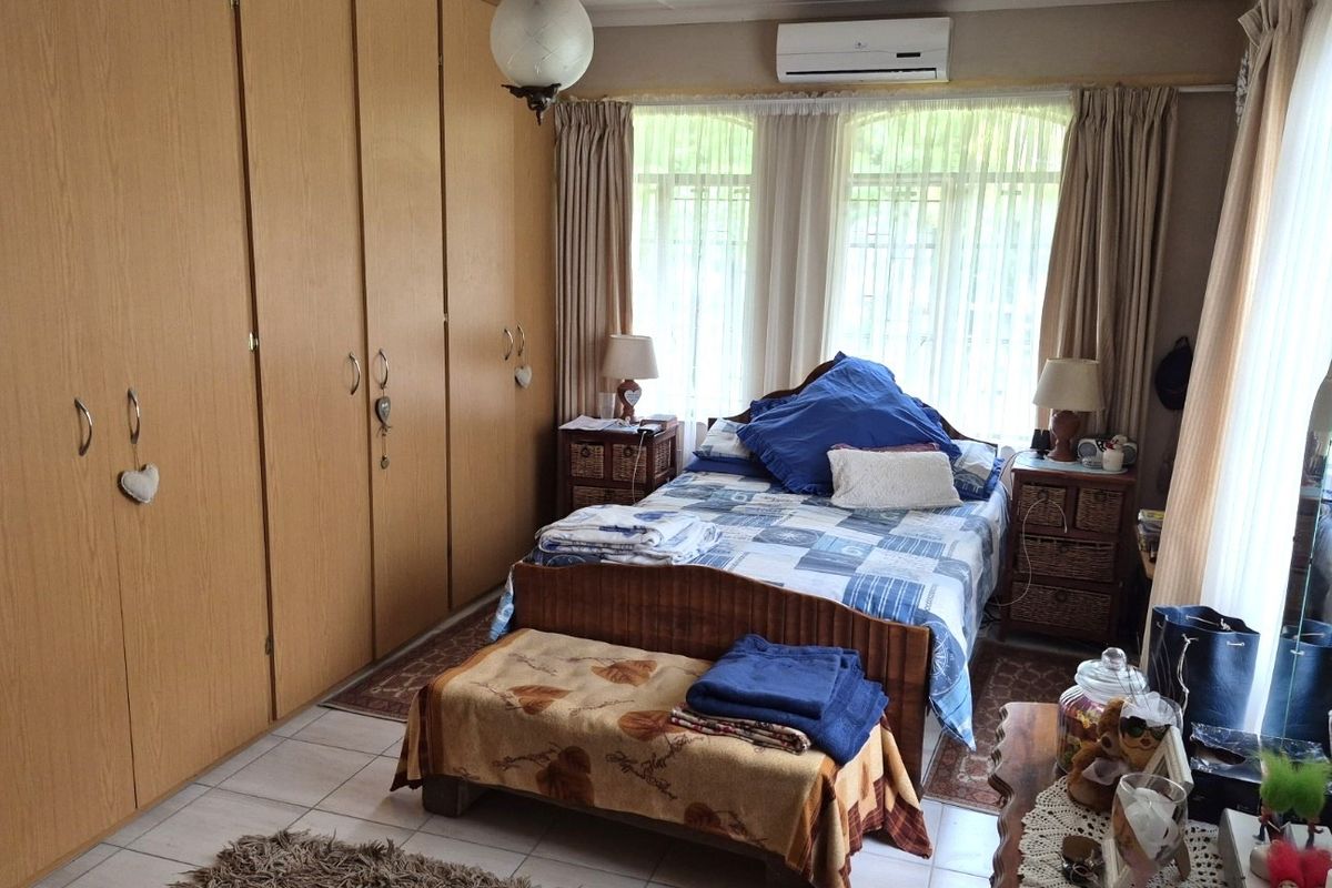 A functional bedroom featuring extensive built-in wooden cupboards, tiled flooring, and a wall-mounted air conditioning unit for climate control.