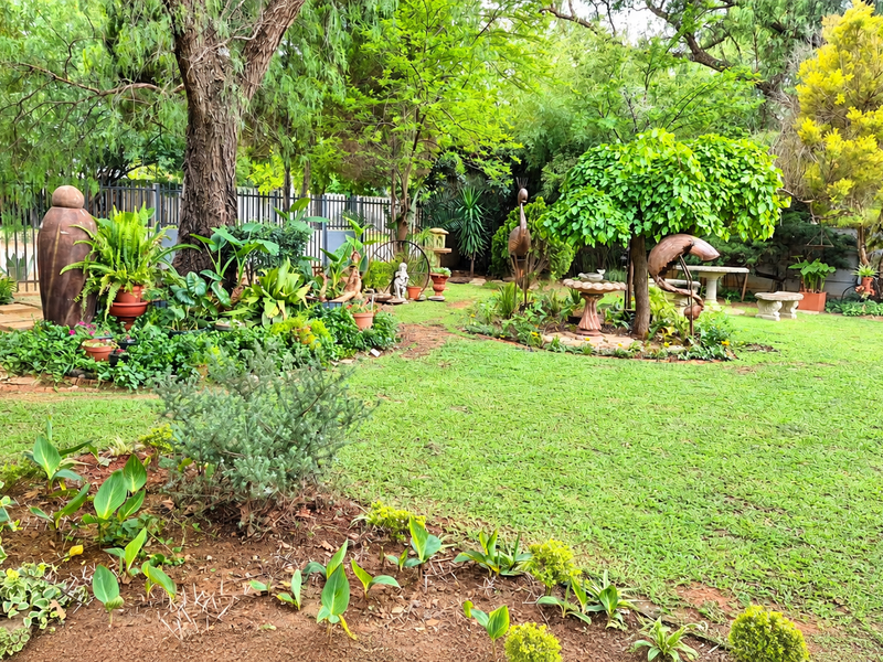 A well-maintained, lush garden featuring mature trees, manicured lawn, and established garden beds with boundary fencing.