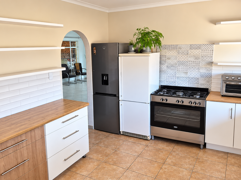 Modern kitchen featuring wooden countertops, white cabinetry, floating shelves, a gas stove with oven, and a decorative tiled backsplash.