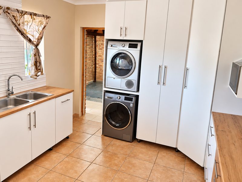 A well-maintained laundry room featuring built-in white cabinetry, wooden countertops, a double stainless steel sink, and stacked laundry appliances.