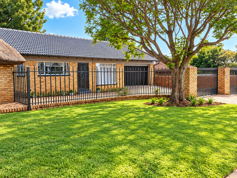 A well-maintained front exterior featuring a combination of thatched and tiled roofing, facebrick walls, secure metal fencing, and a paved driveway.
