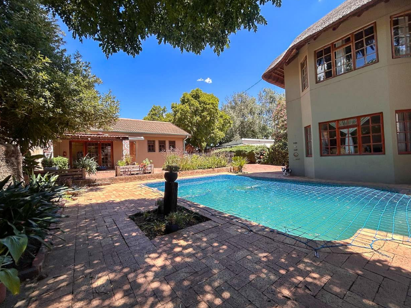 Outdoor pool area featuring a swimming pool with safety net, surrounded by brick paving and a multi-story home with a thatched roof.