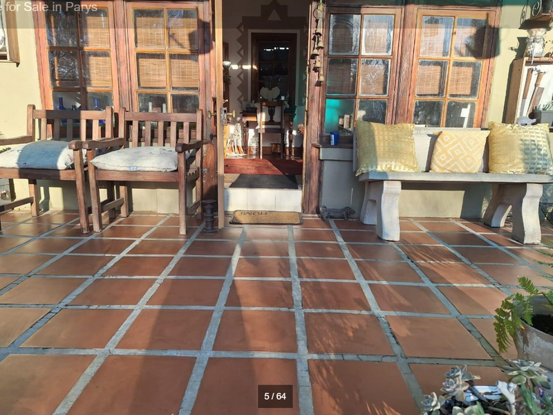 A covered patio area featuring terracotta floor tiles and wooden framed glass doors leading into the home, with a built-in stone bench.