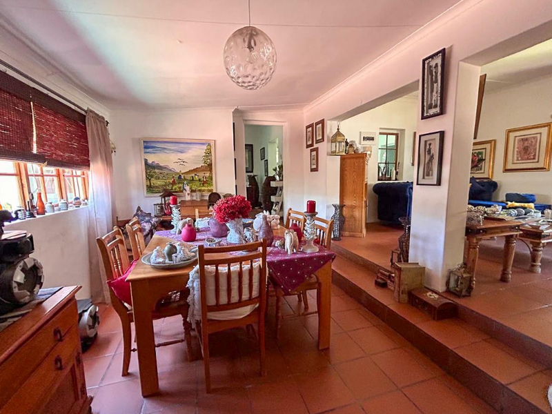 Open-plan dining area featuring terracotta floor tiles, a raised floor transition to the adjacent living space, and classic timber window frames.
