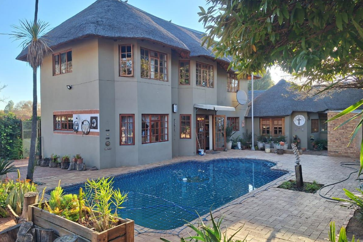 Rear view of a double-story house with a thatched roof, featuring a paved patio area and a swimming pool with a safety net.