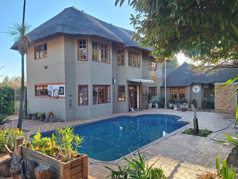 Rear view of a double-story house with a thatched roof, featuring a paved patio area and a swimming pool with a safety net.