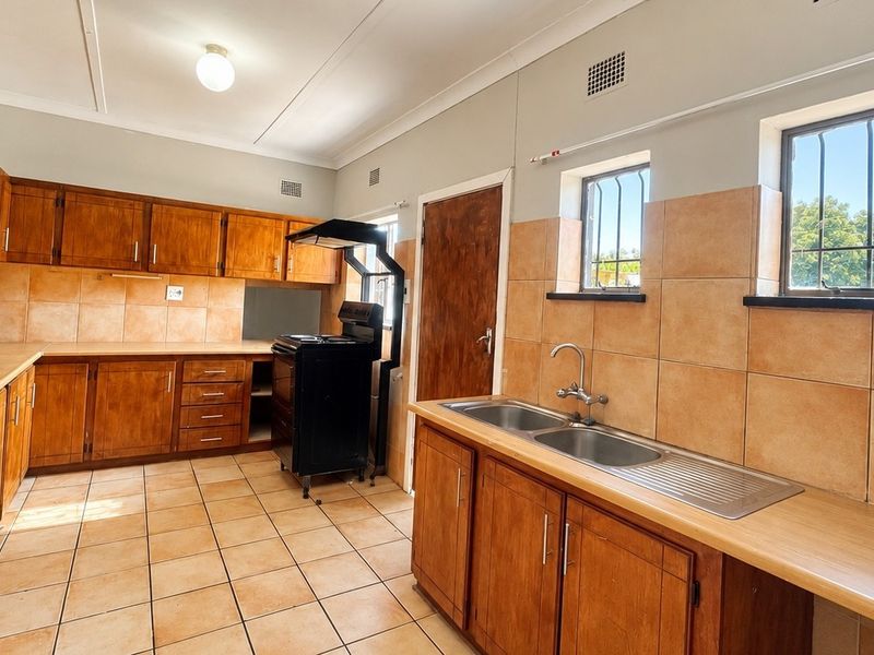 A functional kitchen featuring wooden cabinetry, a double basin sink, tiled splashbacks, and tiled flooring, offering a classic layout ready for modernization.