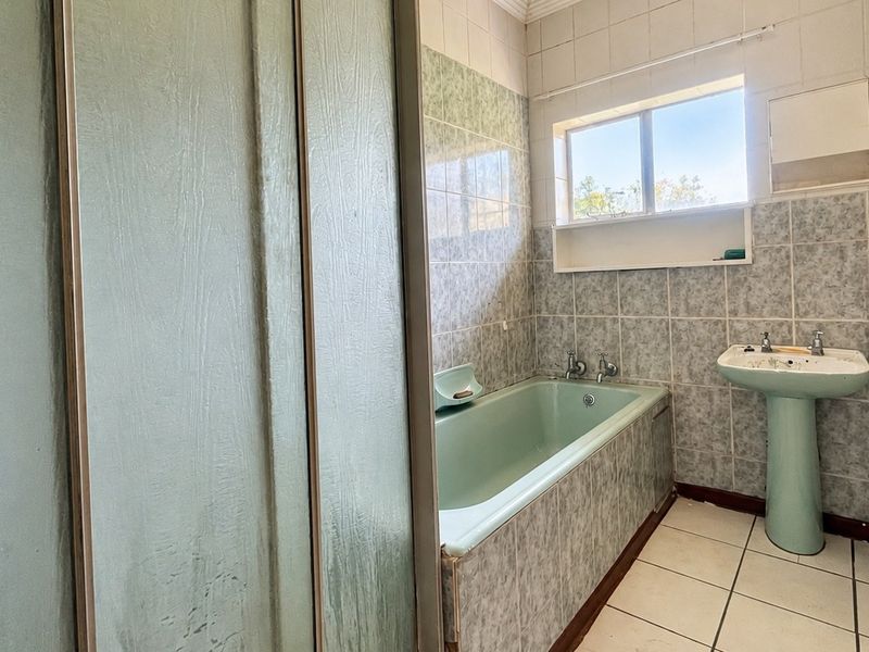 A dated bathroom featuring a pedestal basin, built-in bathtub, and shower enclosure with original tiling, offering potential for a modern renovation.