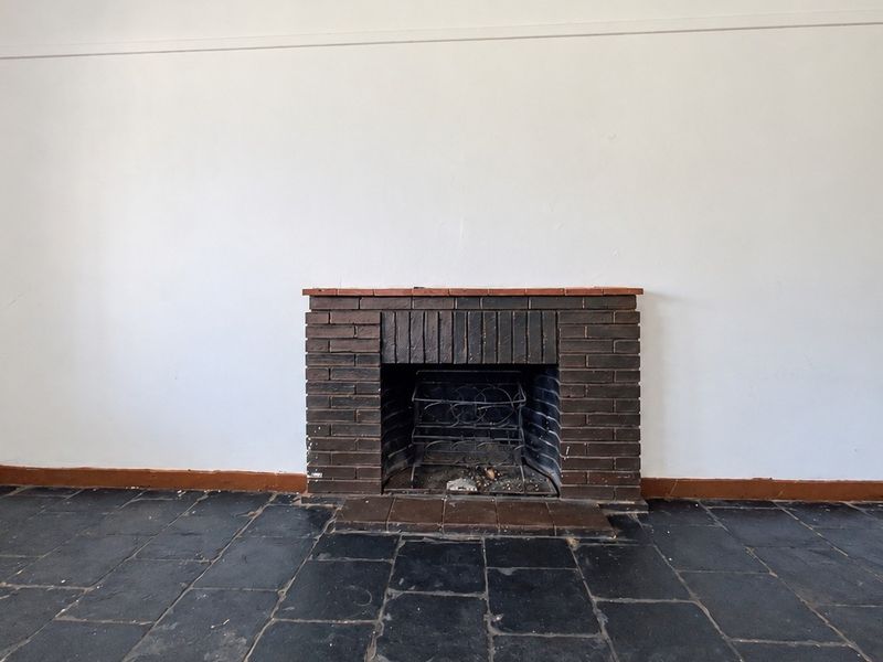 An empty living room featuring a traditional brick fireplace, dark slate tile flooring, and a wall-mounted air conditioning unit.