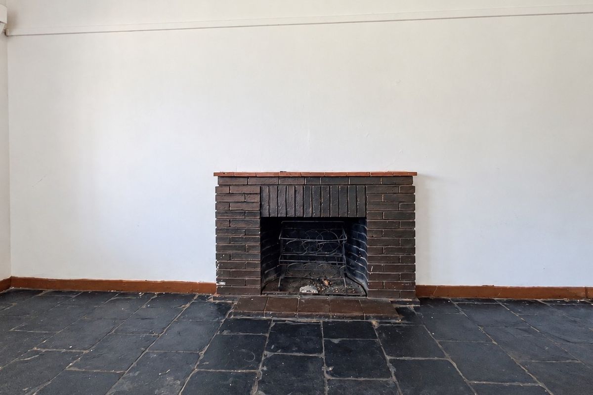An empty living room featuring a traditional brick fireplace, dark slate tile flooring, and a wall-mounted air conditioning unit.