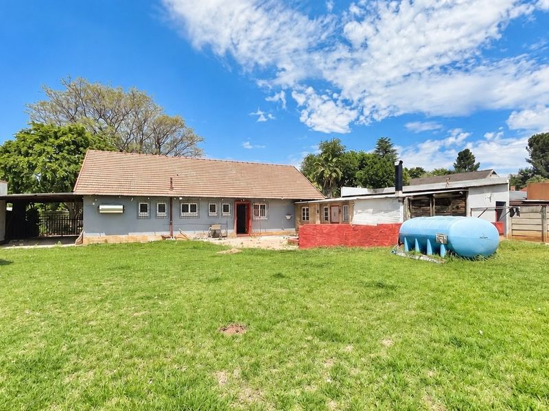 Rear view of the property featuring a large lawn, tiled roof structure, and an external gas storage tank.