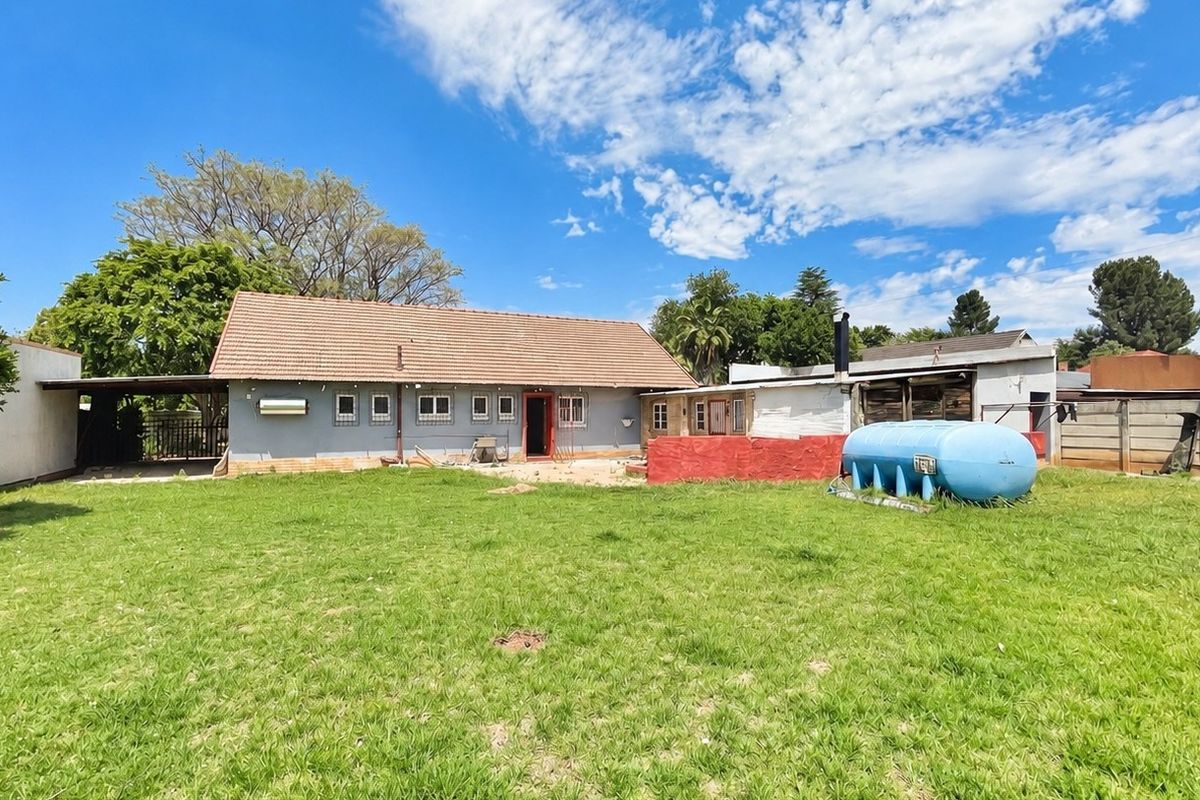 Rear view of the property featuring a large lawn, tiled roof structure, and an external gas storage tank.