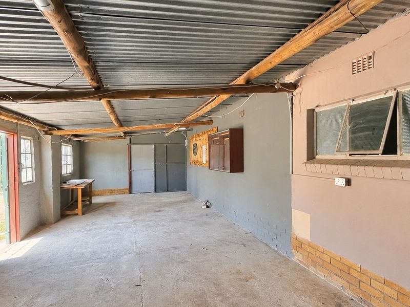 A spacious, unfinished garage area featuring exposed timber rafters, corrugated metal roofing, and concrete flooring, offering potential for workshop or storage use.