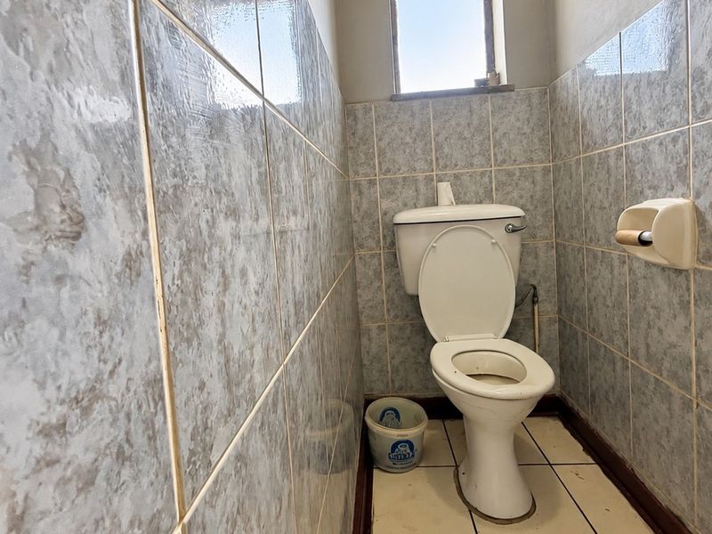 A compact bathroom featuring ceramic wall and floor tiling, equipped with a standard toilet and a small window for natural light.