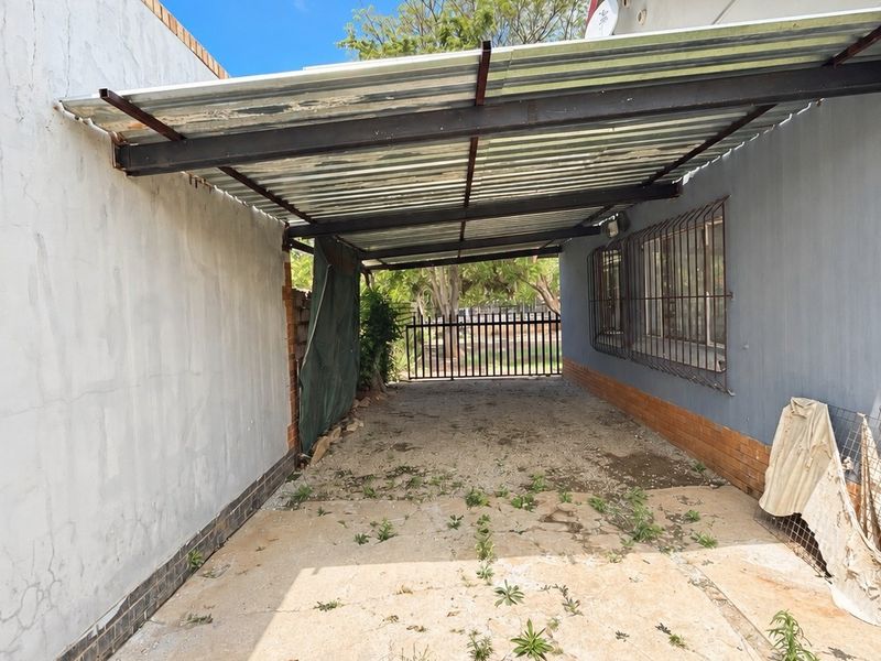 A covered outdoor parking area or carport featuring a corrugated metal roof, concrete flooring, and secure gated access.
