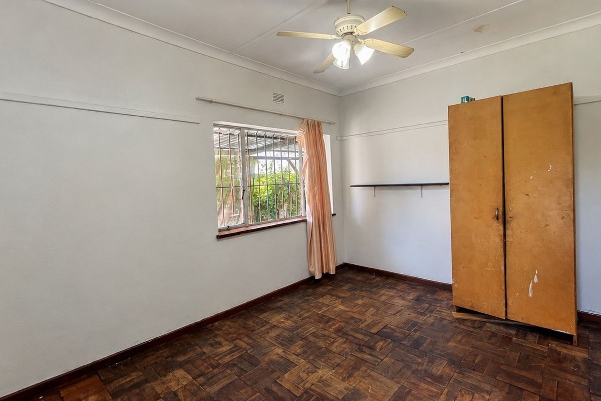 A bedroom featuring original parquet flooring, a ceiling fan, and security bars on the window, offering a blank canvas for renovation.