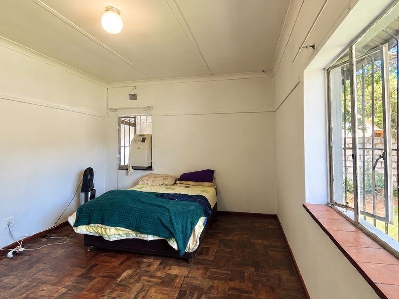 A bedroom featuring parquet flooring, security bars on the windows, and a tiled window sill, offering a functional space with potential for cosmetic updates.