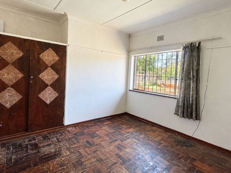 A vacant bedroom featuring original parquet flooring, a built-in wooden wardrobe, and a window fitted with security bars.