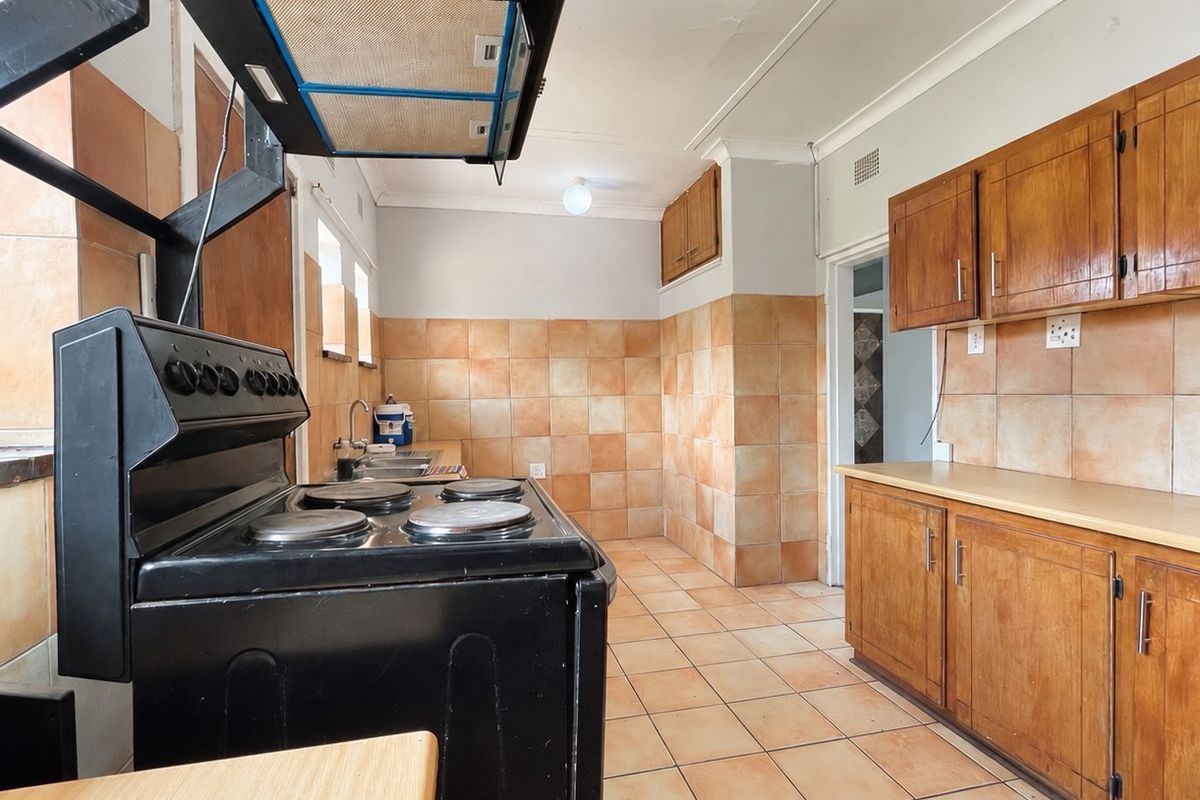 A functional kitchen featuring wooden cabinetry, tiled splashbacks, and a freestanding stove, offering a dated aesthetic with potential for modern renovation.