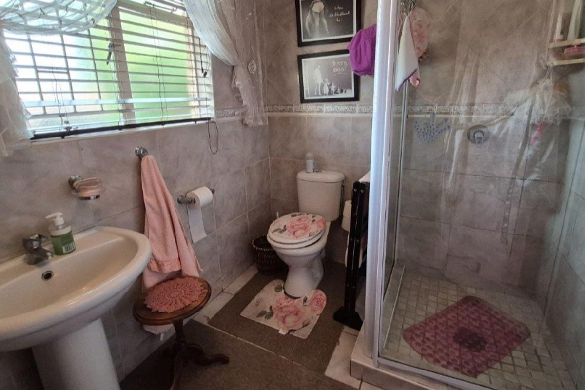 A functional bathroom featuring a pedestal basin, toilet, and a glass-enclosed shower with neutral wall and floor tiling.