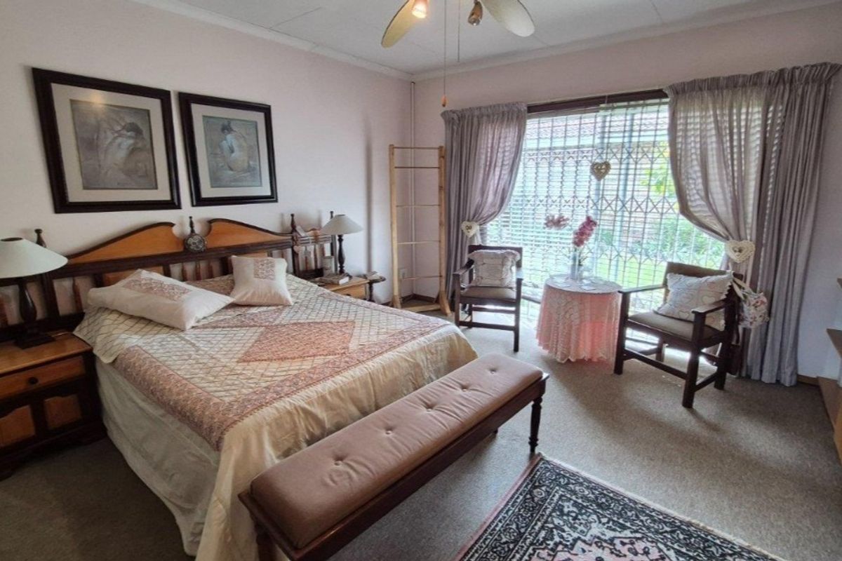 A spacious bedroom featuring a ceiling fan, built-in shelving, and a large window with an integrated security gate overlooking the garden.