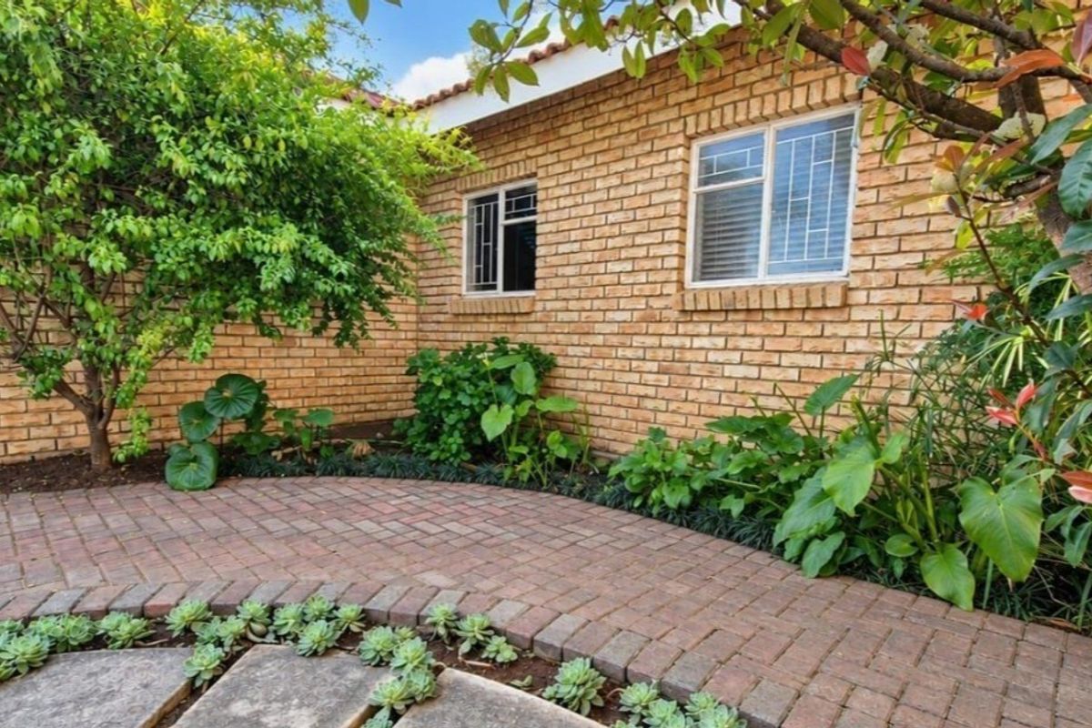 A well-maintained rear exterior view featuring a brick facade, paved patio area, and established garden landscaping.