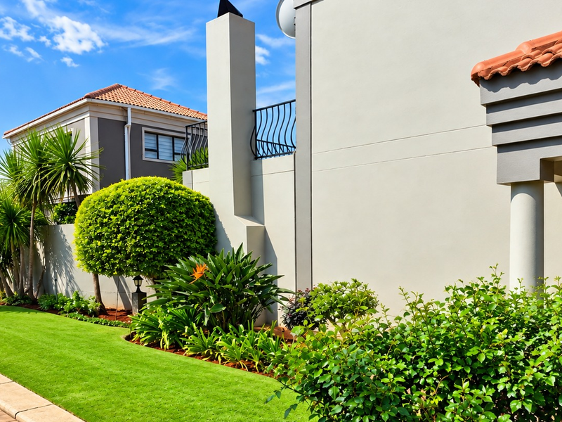 A well-maintained rear exterior view of the townhouse featuring a manicured lawn, landscaped garden, paved walkway, and a prominent external chimney.