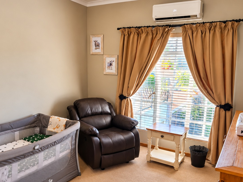 A well-maintained bedroom featuring neutral wall tones, carpeted flooring, and a wall-mounted split-system air conditioning unit.