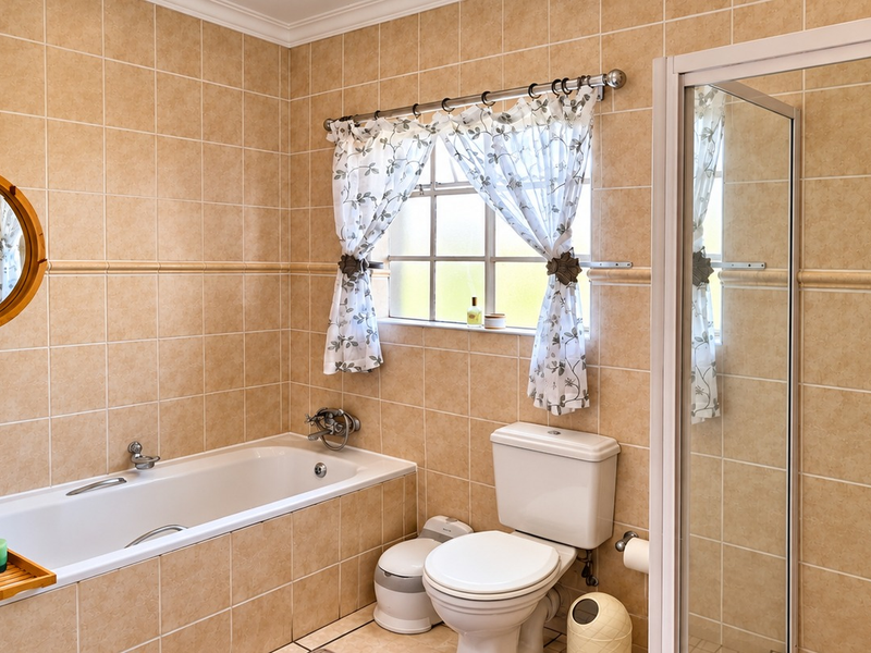 A functional bathroom featuring full-height wall tiling, a built-in bathtub, a separate shower enclosure, and a standard toilet.