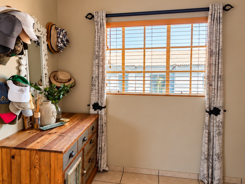 A well-lit bedroom featuring tiled flooring, a wooden window frame with venetian blinds, and decorative curtain rods.