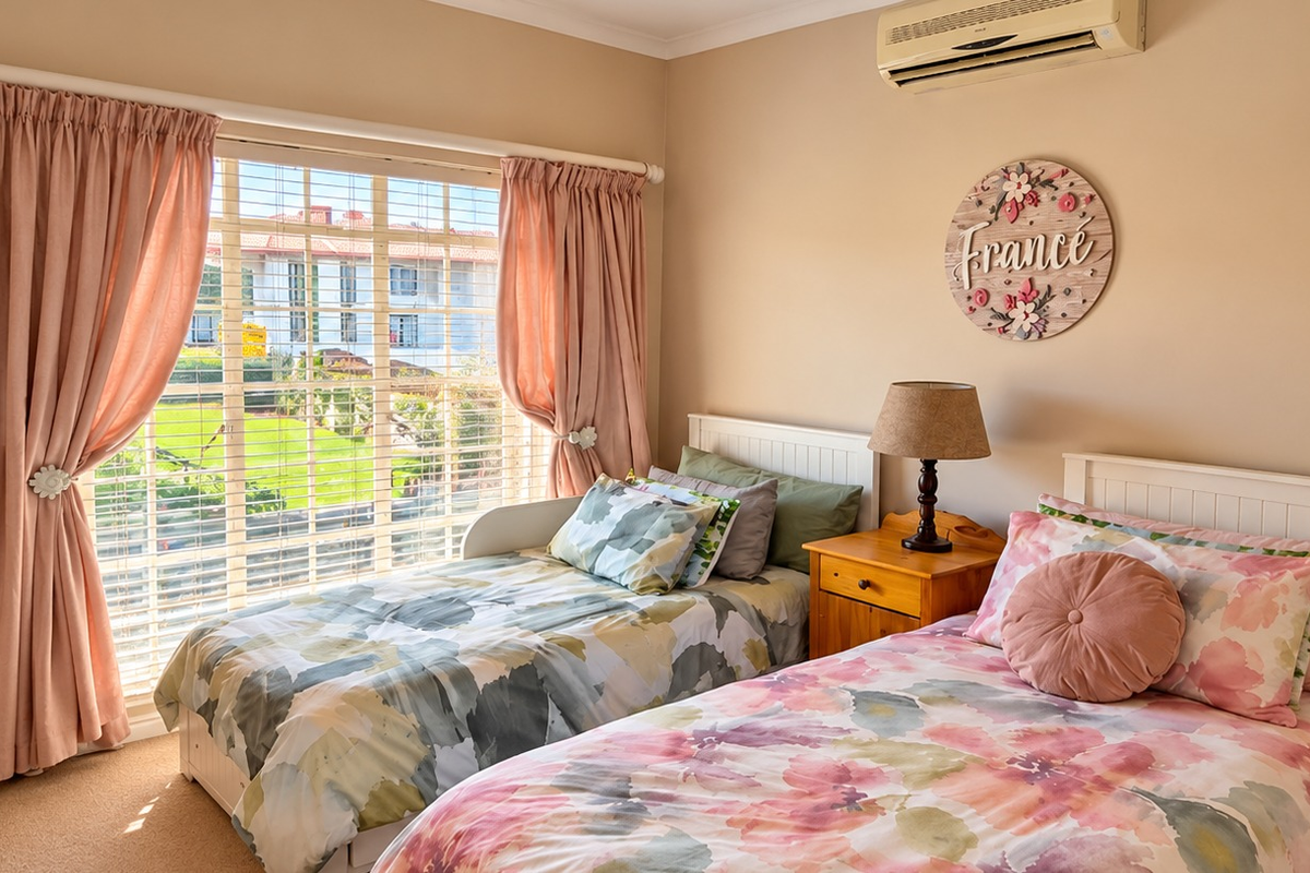 A well-maintained bedroom featuring carpeted flooring, a wall-mounted split-system air conditioner, and large windows with blinds and curtains overlooking the exterior.