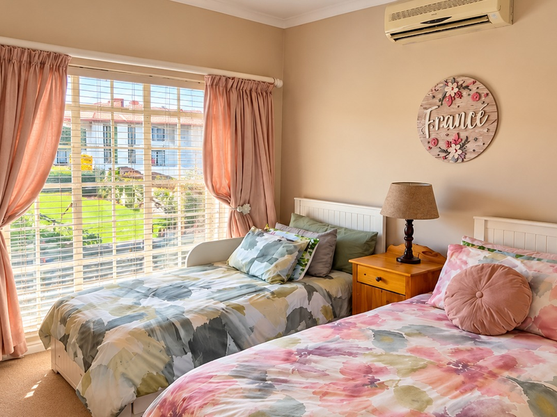 A well-maintained bedroom featuring carpeted flooring, a wall-mounted split-system air conditioner, and large windows with blinds and curtains overlooking the exterior.