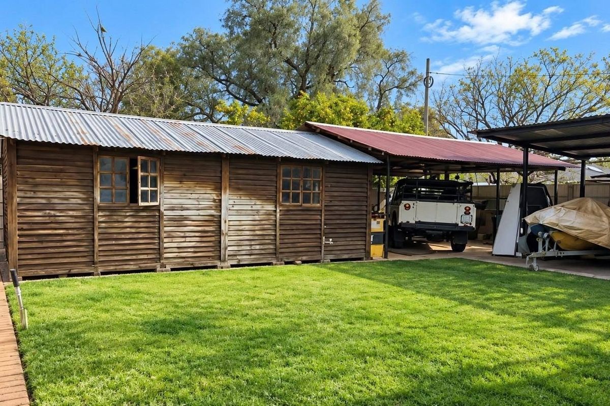 A detached timber-clad outbuilding featuring a corrugated metal roof and an attached carport, situated in a residential backyard.