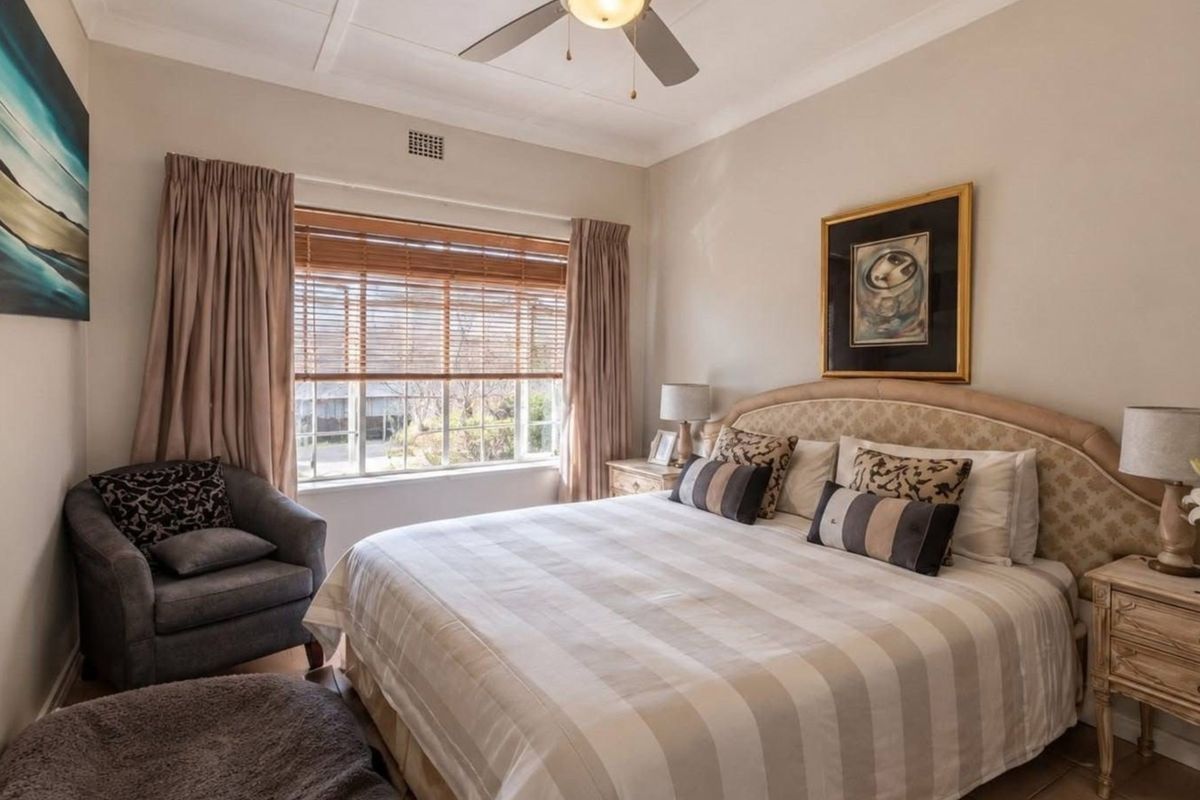 A well-maintained bedroom featuring a ceiling fan, coved cornicing, and timber venetian blinds, offering a comfortable and functional living space.