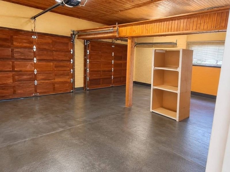 Spacious double garage featuring timber ceiling, painted brick walls, and a clean concrete floor with two wooden garage doors.