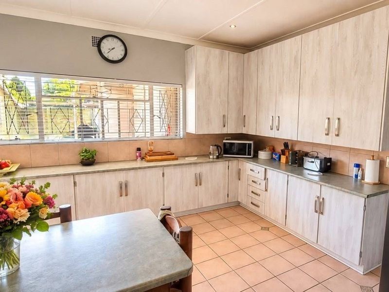 A functional kitchen featuring light-toned laminate cabinetry, tiled backsplash, and ceramic floor tiles, offering ample storage and workspace with natural light from the window.