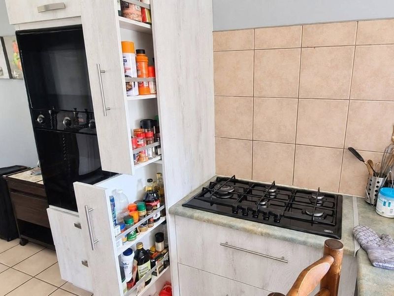 A functional kitchen area featuring a built-in oven, gas hob, tiled backsplash, and a convenient pull-out pantry cupboard for organized storage.