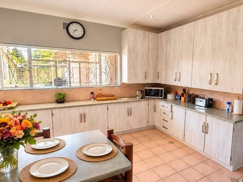 A functional kitchen featuring light-toned built-in cabinetry, laminate countertops, tiled backsplash, and tiled flooring, with a large window providing natural light.