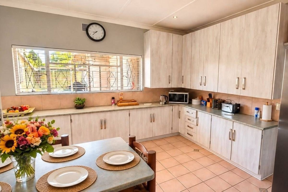 A functional kitchen featuring light-toned built-in cabinetry, laminate countertops, tiled backsplash, and tiled flooring, with a large window providing natural light.