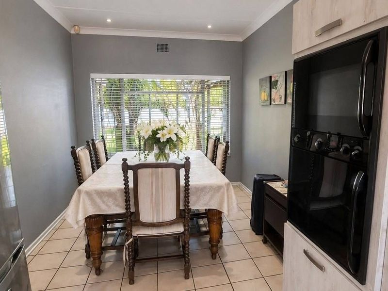 A dining room featuring tiled flooring, recessed downlights, and a built-in oven, with natural light entering through a window fitted with venetian blinds.