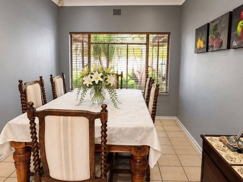 A functional dining room featuring neutral grey walls, tiled flooring, and a large window with wooden blinds, providing a bright and comfortable space.