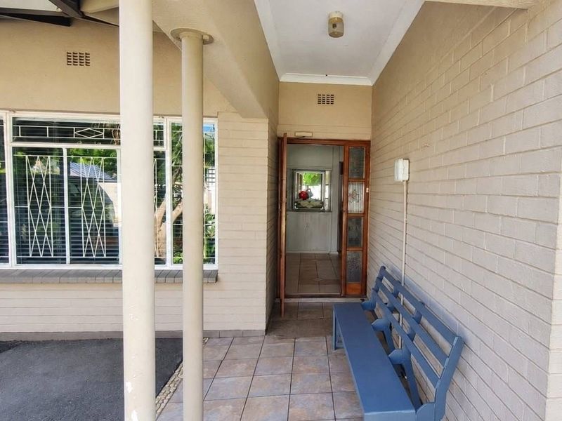 A covered patio area featuring tiled flooring, brick walls, and security bars on the windows, providing a sheltered entrance to the home.