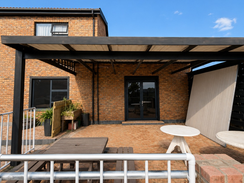 A covered outdoor patio area featuring brick wall construction, paved flooring, and a black metal roof structure, providing a functional exterior space.