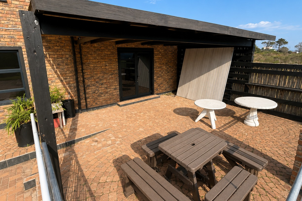 A covered outdoor patio area featuring brick paving, an exposed brick facade, and a timber pergola structure.