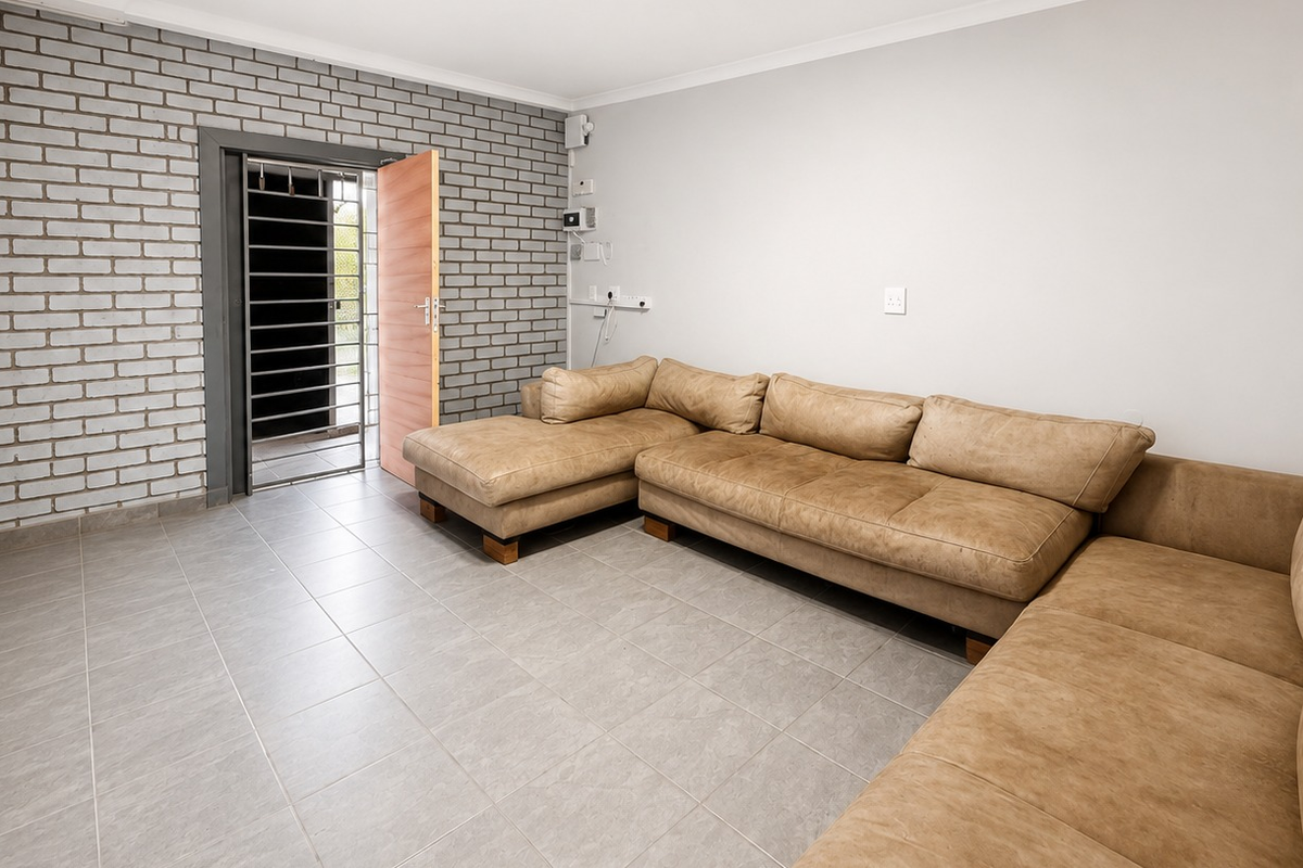 A functional office space featuring durable tiled flooring, an exposed brick feature wall, and a secure entrance with a fitted security gate.